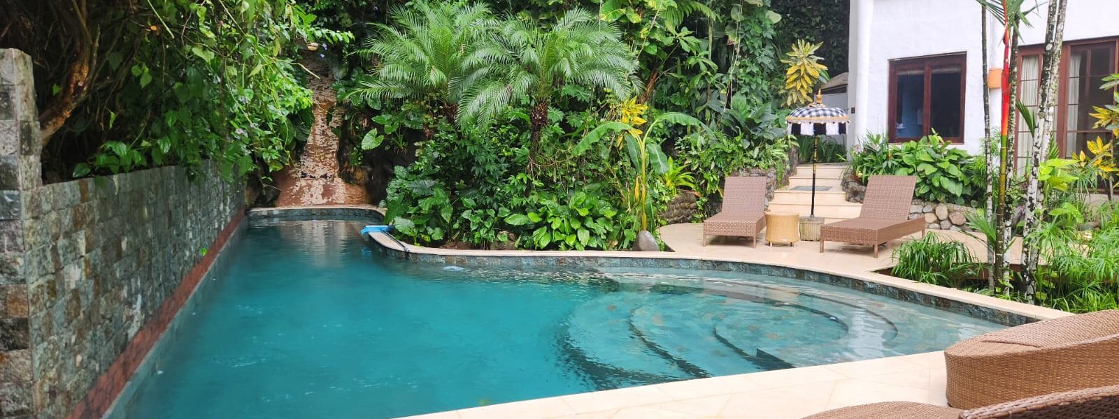 The pool area is surrounded by a perfectly-maintained garden full of lush vibrant tropical plants. 